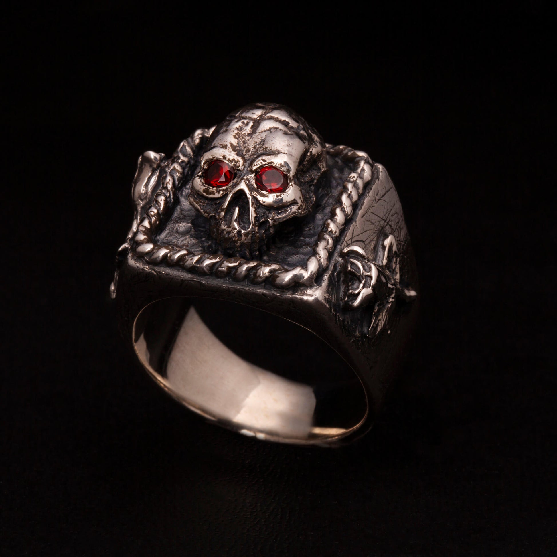Anello chevalier in argento 925 con teschio tridimensionale e steli di rosa sui gambi laterali. Granati incastonati nelle orbite.