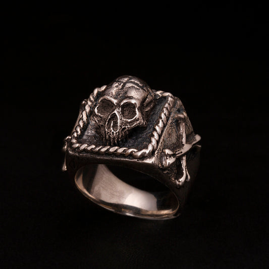 Anello chevalier in argento 925 con teschio tridimensionale e ossa incrociate sui gambi laterali.