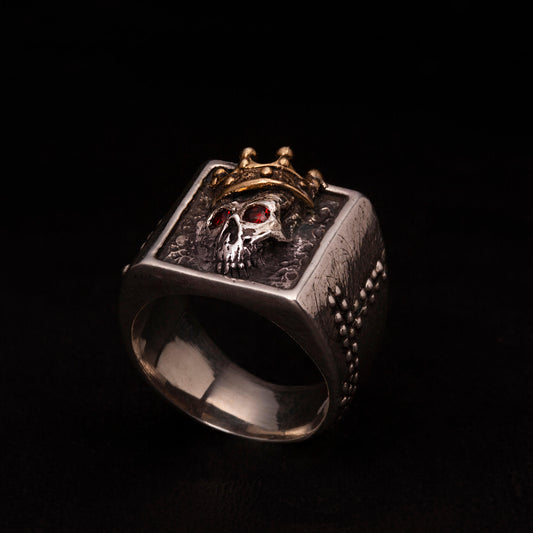 Anello in argento925 con teschio e corona in ottone. Granati incastonati nelle orbite e gambi rivettati.