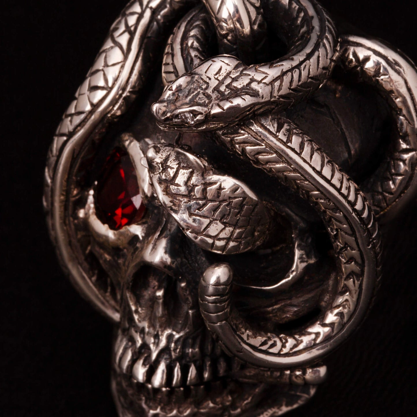 Anello in argento 925 con teschio anatomico e due serpenti avvolti. Impreziosito con diamanti naturali e granato.