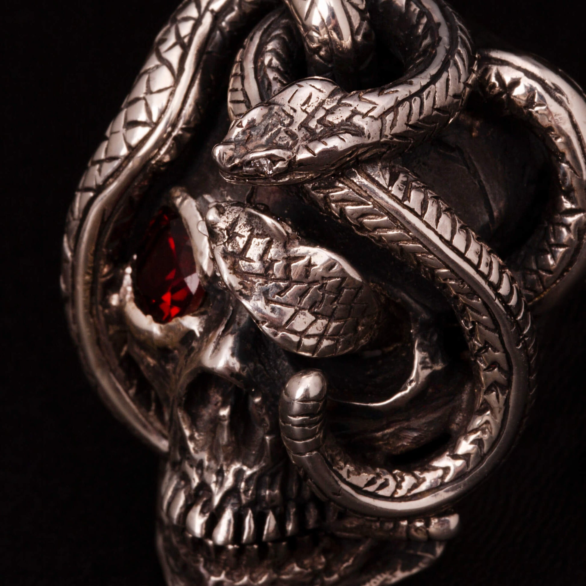 Anello in argento 925 con teschio anatomico e due serpenti avvolti. Impreziosito con diamanti naturali e granato.