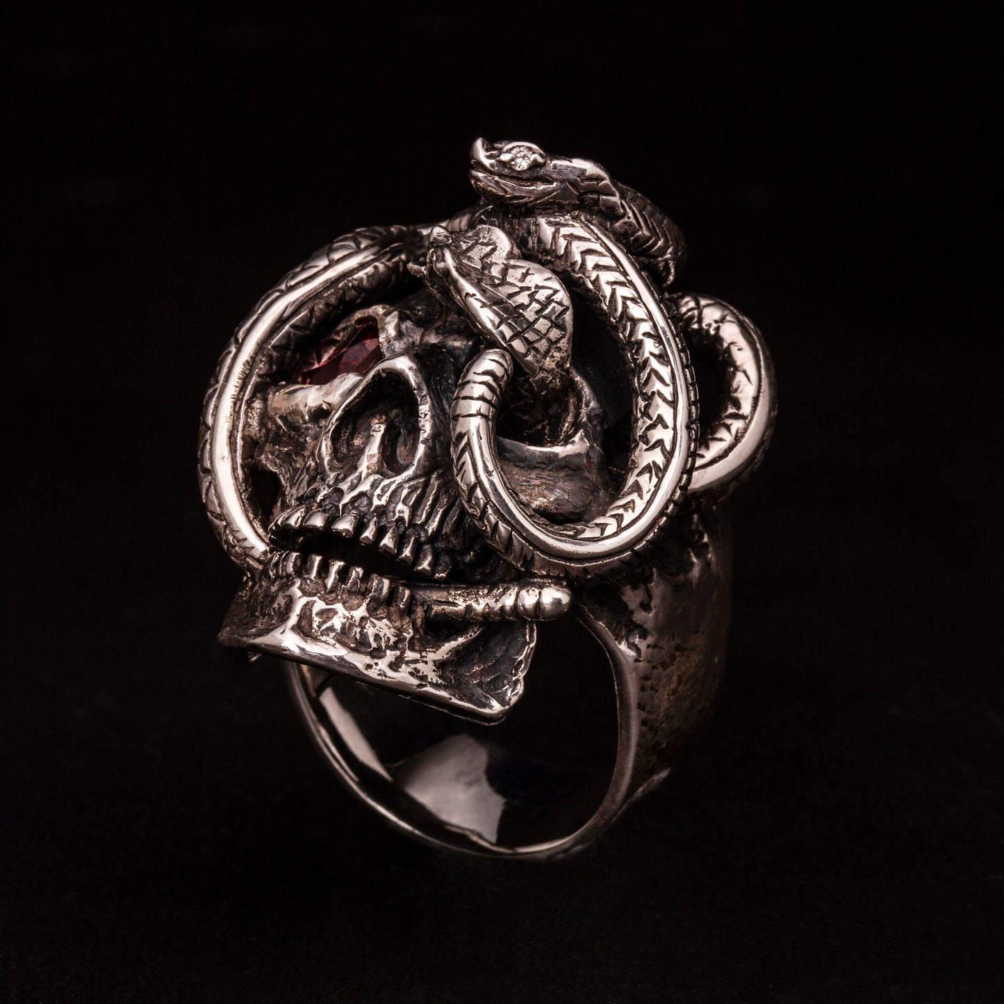 Anello in argento 925 con teschio anatomico e due serpenti avvolti. Impreziosito con diamanti naturali e granato.