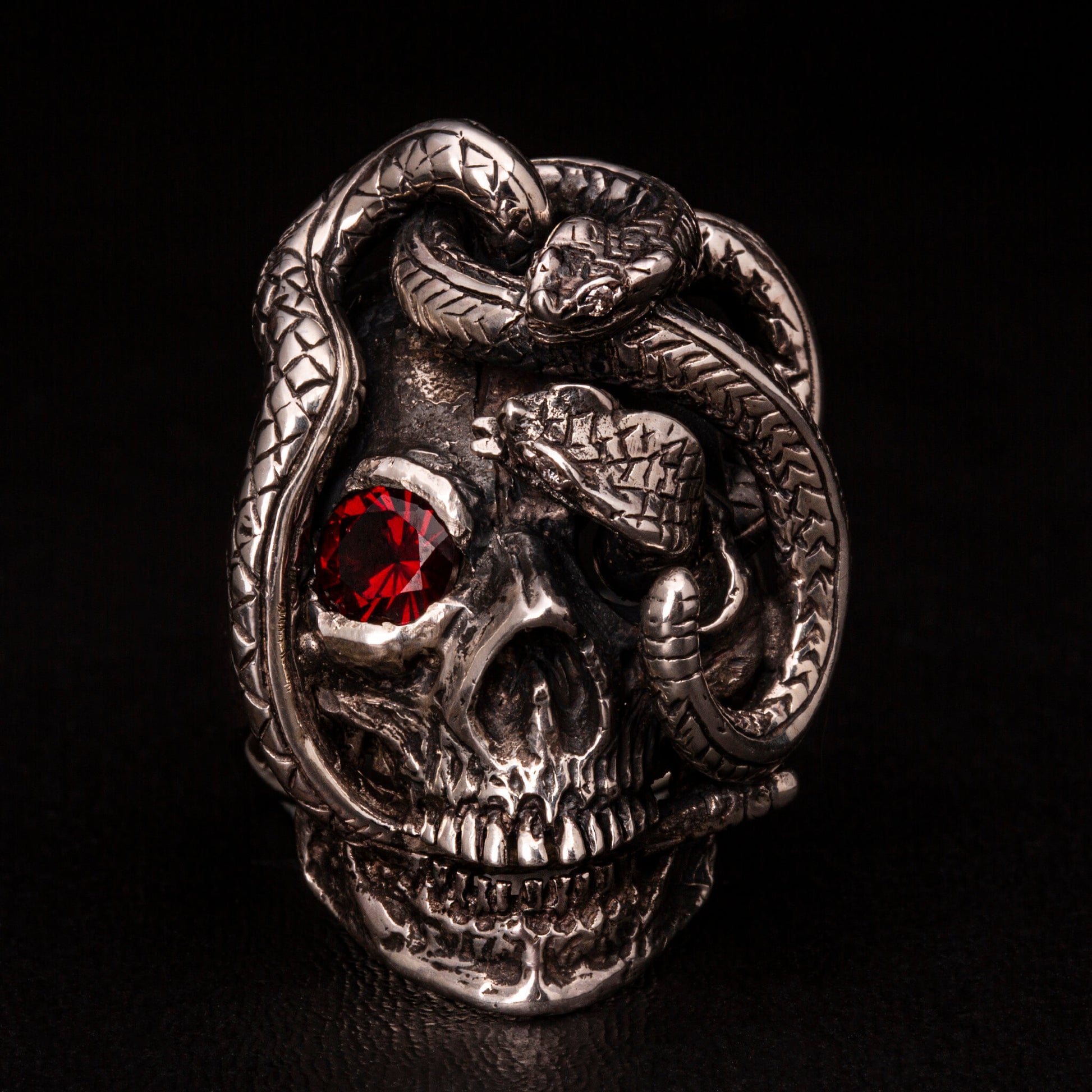 Anello in argento 925 con teschio anatomico e due serpenti avvolti. Impreziosito con diamanti naturali e granato.