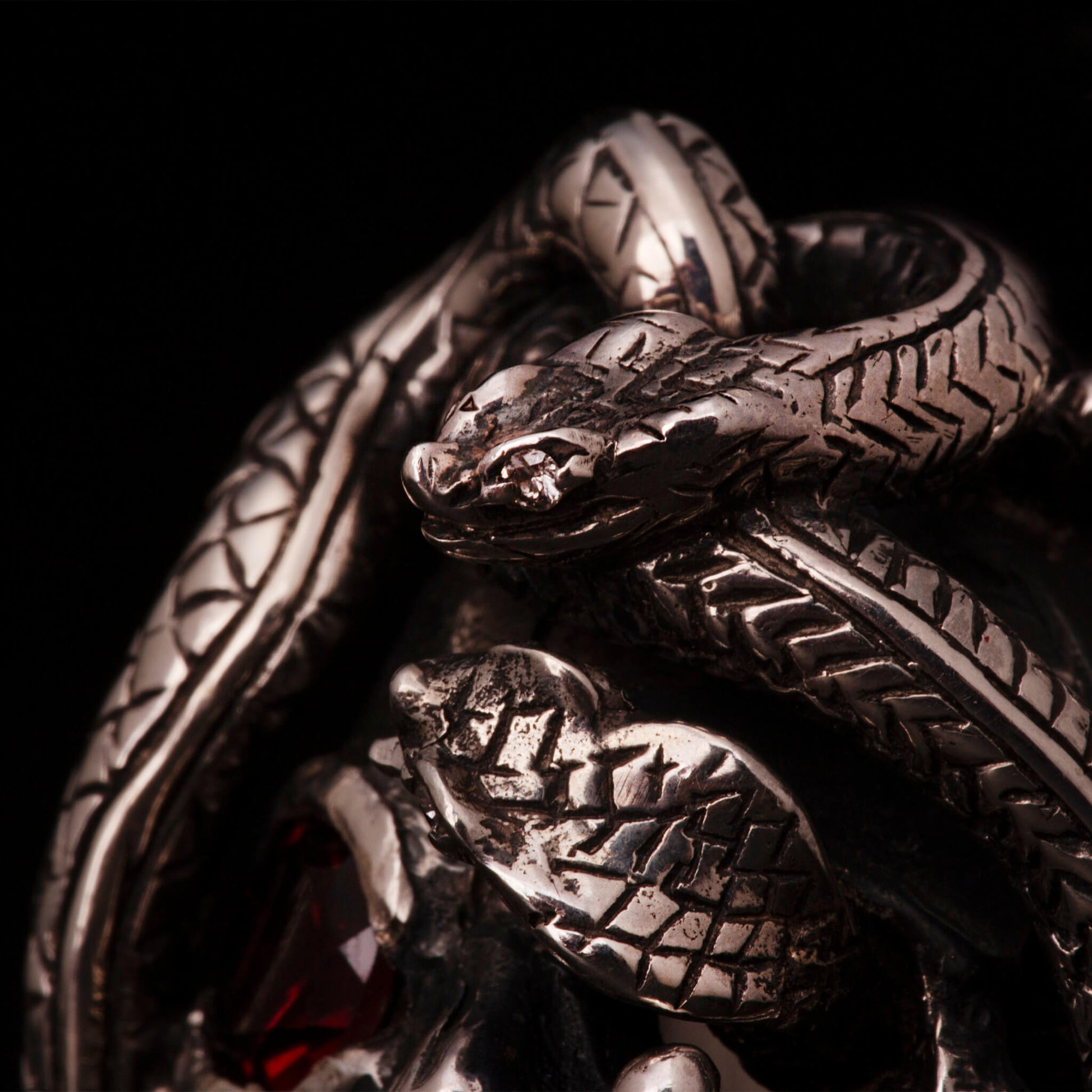 Anello in argento 925 con teschio anatomico e due serpenti avvolti. Impreziosito con diamanti naturali e granato.