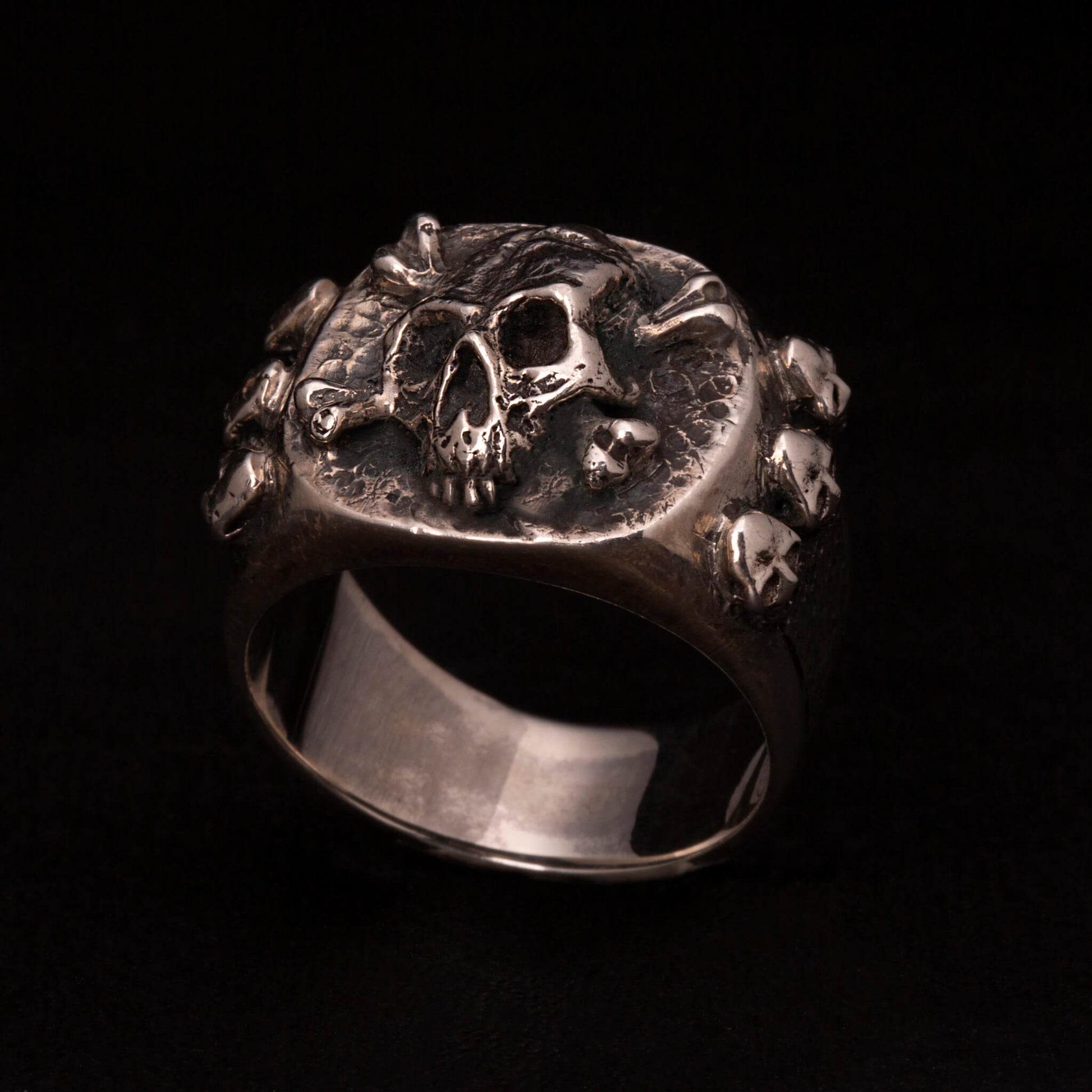 Anello chevalier in argento 925 con teschio e ossa incrociate. Sei micro teschietti impreziosiscono i gambi laterali.