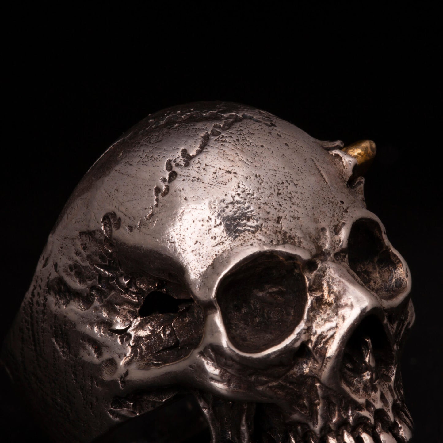 Anello in argento925 con teschio anatomico e pallottola in ottone con dettaglio del foro di entrata sul cranio.