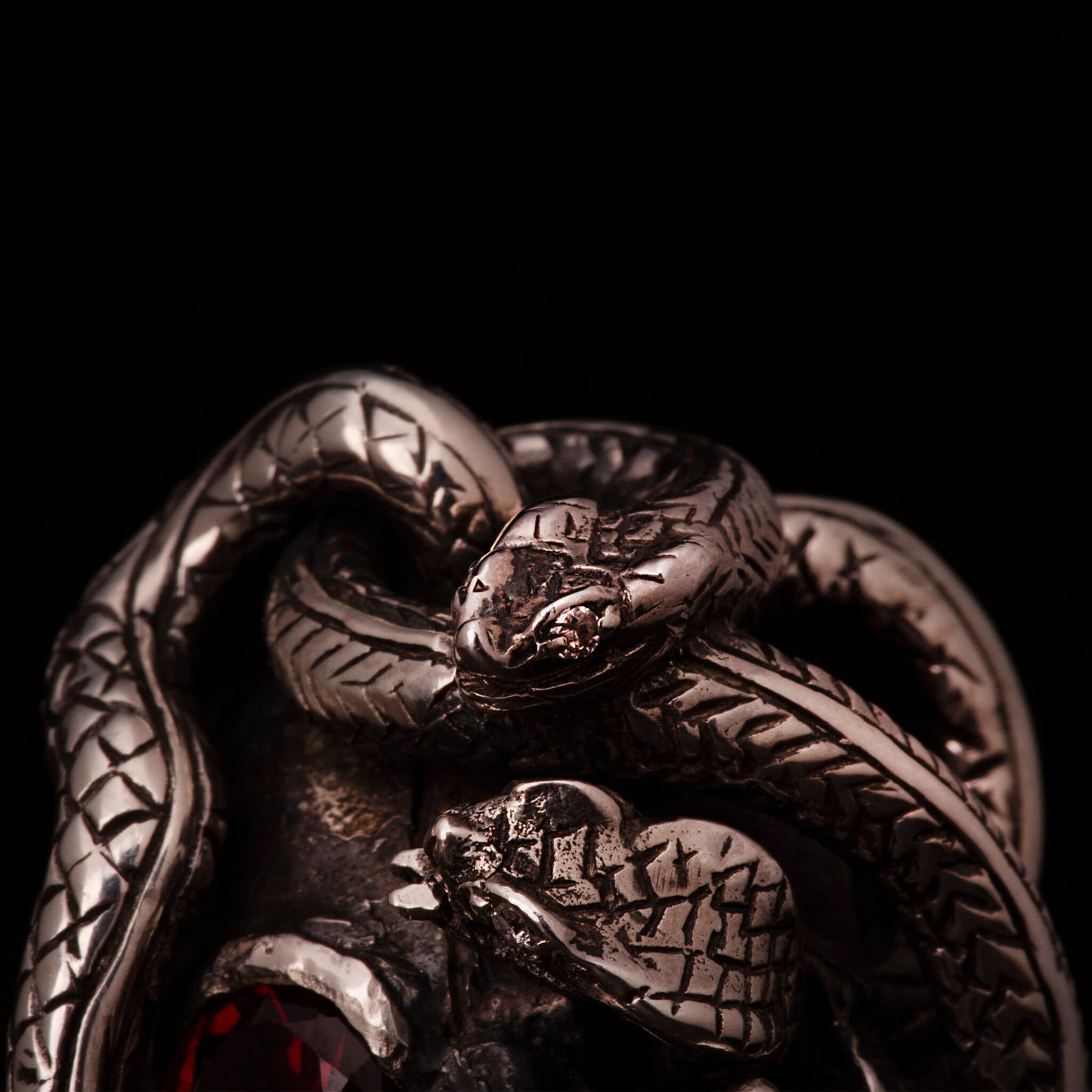Anello in argento 925 con teschio anatomico e due serpenti avvolti. Impreziosito con diamanti naturali e granato.