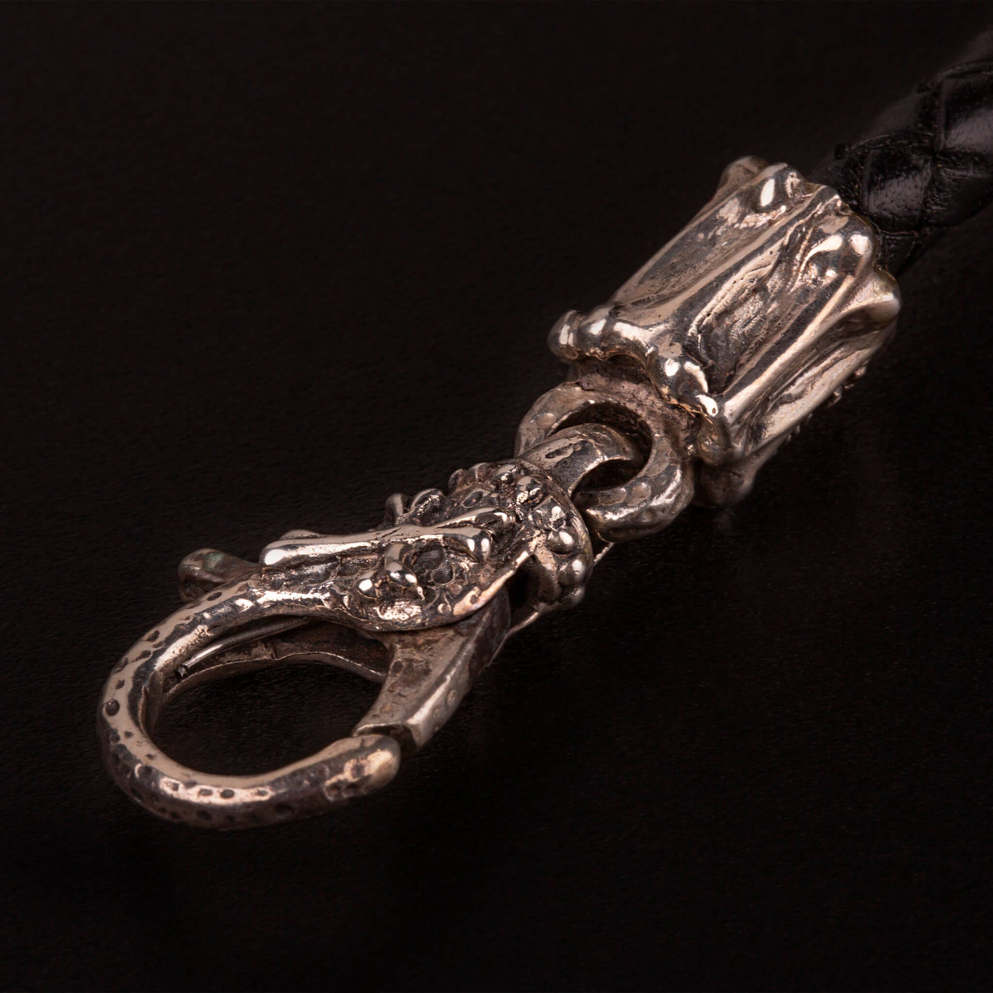 Bracciale con piastrina e teschi ai lati in argento925, cinturino in pelle nera intrecciata e moschettone lavorato in argento925.