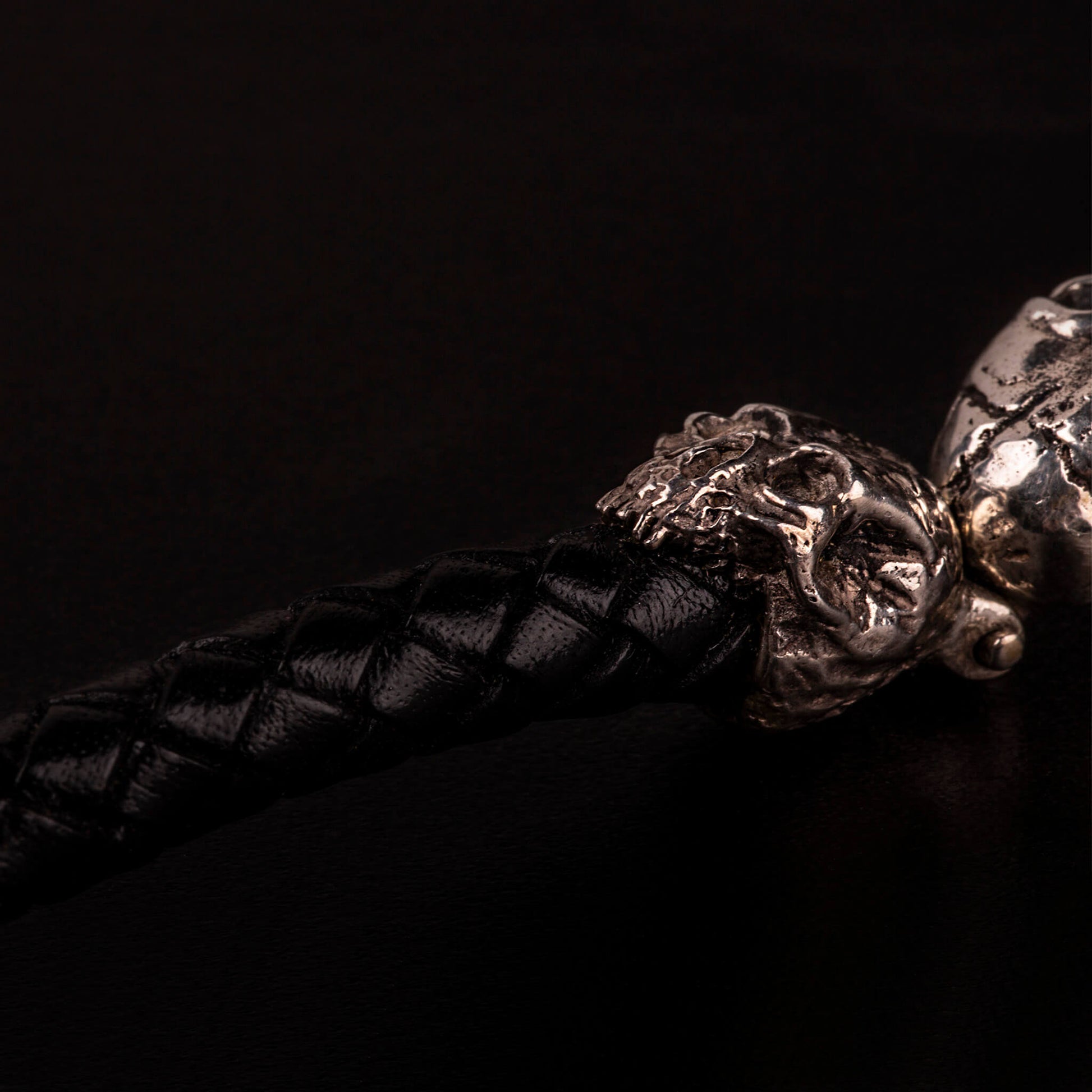 Bracciale con piastrina e teschi ai lati in argento925, cinturino in pelle nera intrecciata e moschettone lavorato in argento925.