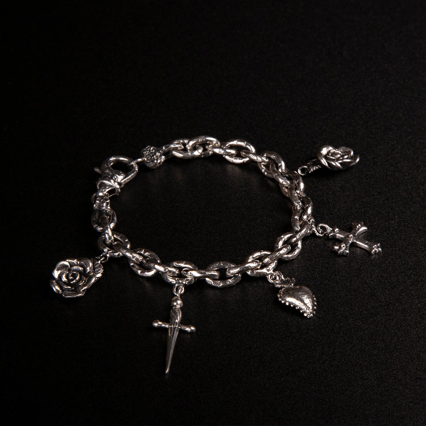 Bracciale in argento925 con maglie rolo' effetto ribattuto e charms raffiguranti rosa, pugnale, cuore votivo e croce gotica.