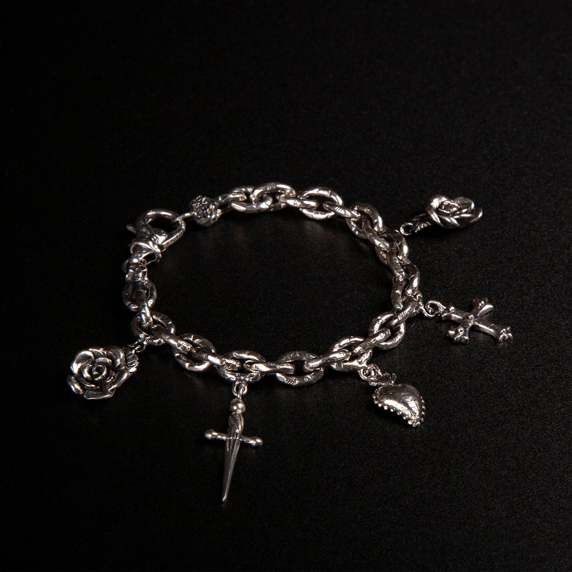 Bracciale in argento925 con maglie rolo' effetto ribattuto e charms raffiguranti rosa, pugnale, cuore votivo e croce gotica.