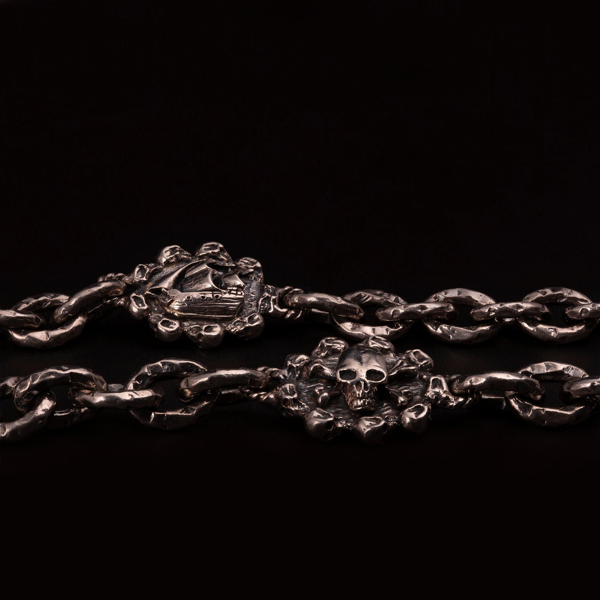Catena portafoglio in argento925 con maglia rolo ribattuta e due medagliette con veliero e teschio pirata in rilievo. Moschettone con ossa incrociate e teschi e pendenti ruota con ala e teschio.