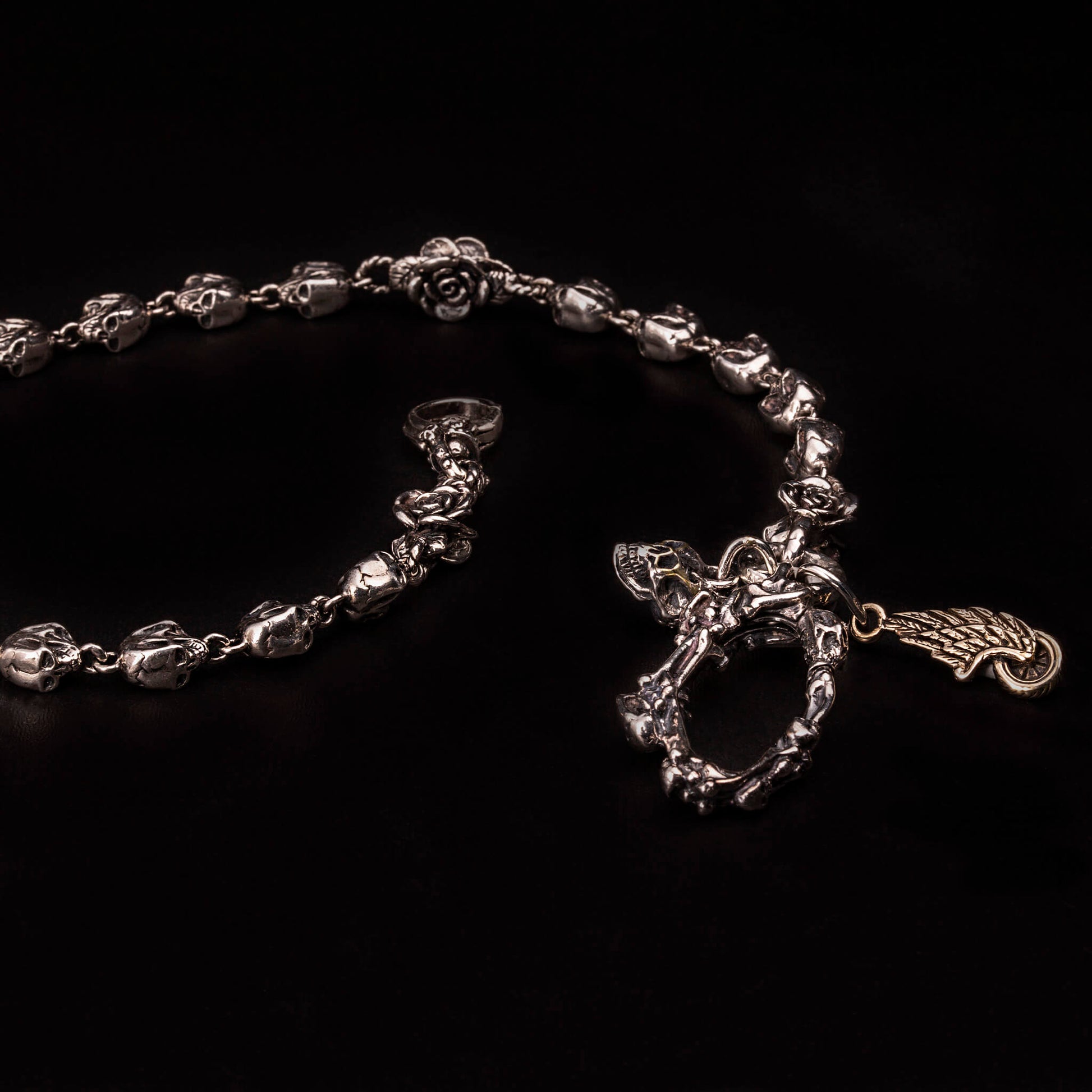 Catena portafoglio in argento925 con teschi e rose. Moschettone a molla formato da ossa incrociate e piccoli teschi.Legati come pendenti al moschettone un teschio e ruota con ala.