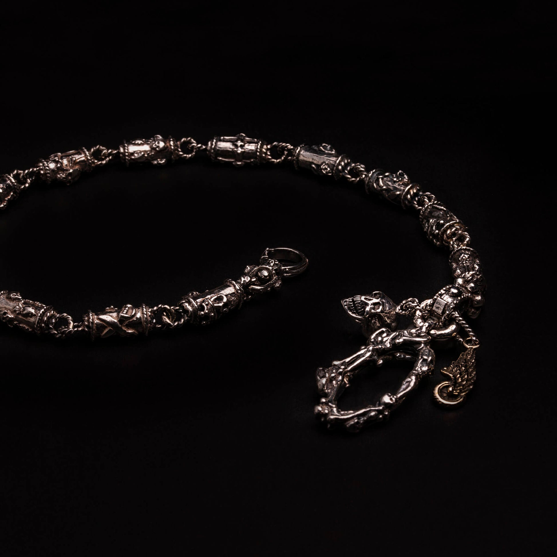 Catena portafoglio n argento925 con elementi tubolari decorati con teschi, cuori votivi, croci gotiche. Moschettone composto da ossa incrociate e teschi, con targhetta ruota e ala e teschio.