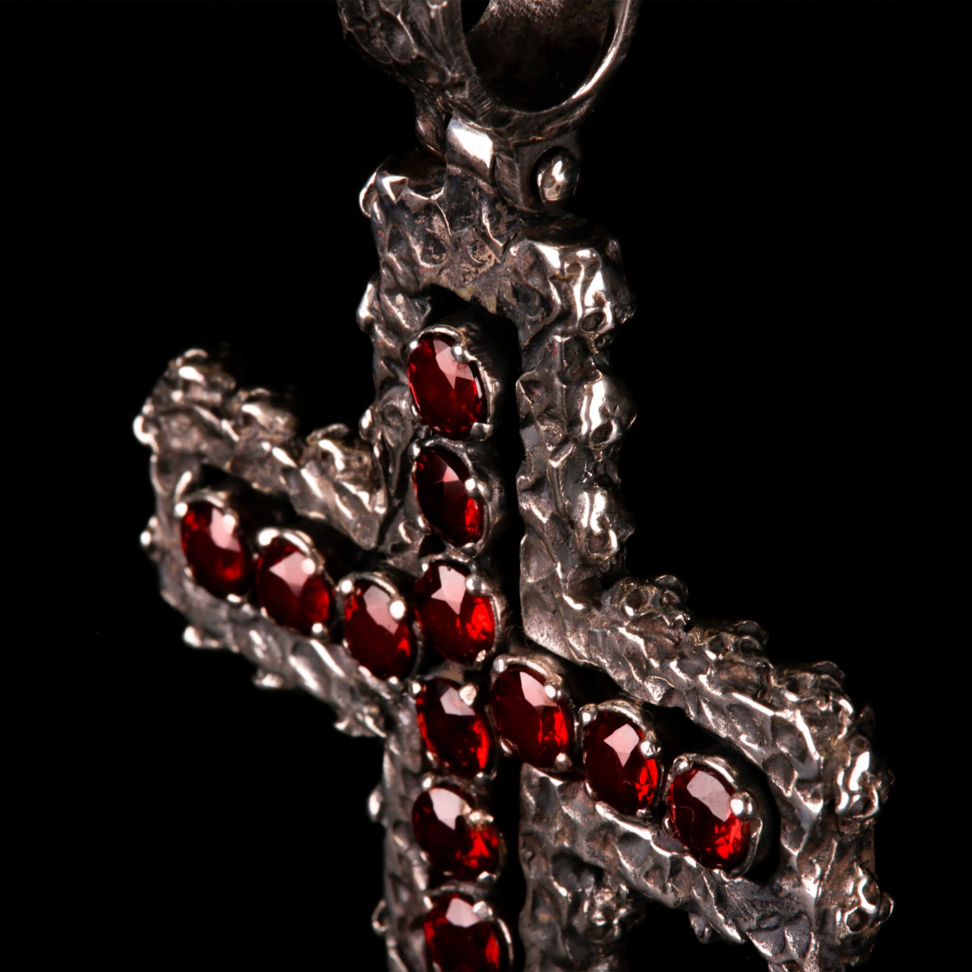 Crux Reliqvia e' un pendente a forma di croce con superficie scalfita irregolare, micro teschi saldati lungo lo spessore e incastonati granati naturali in tutta lunghezza e largezza.
