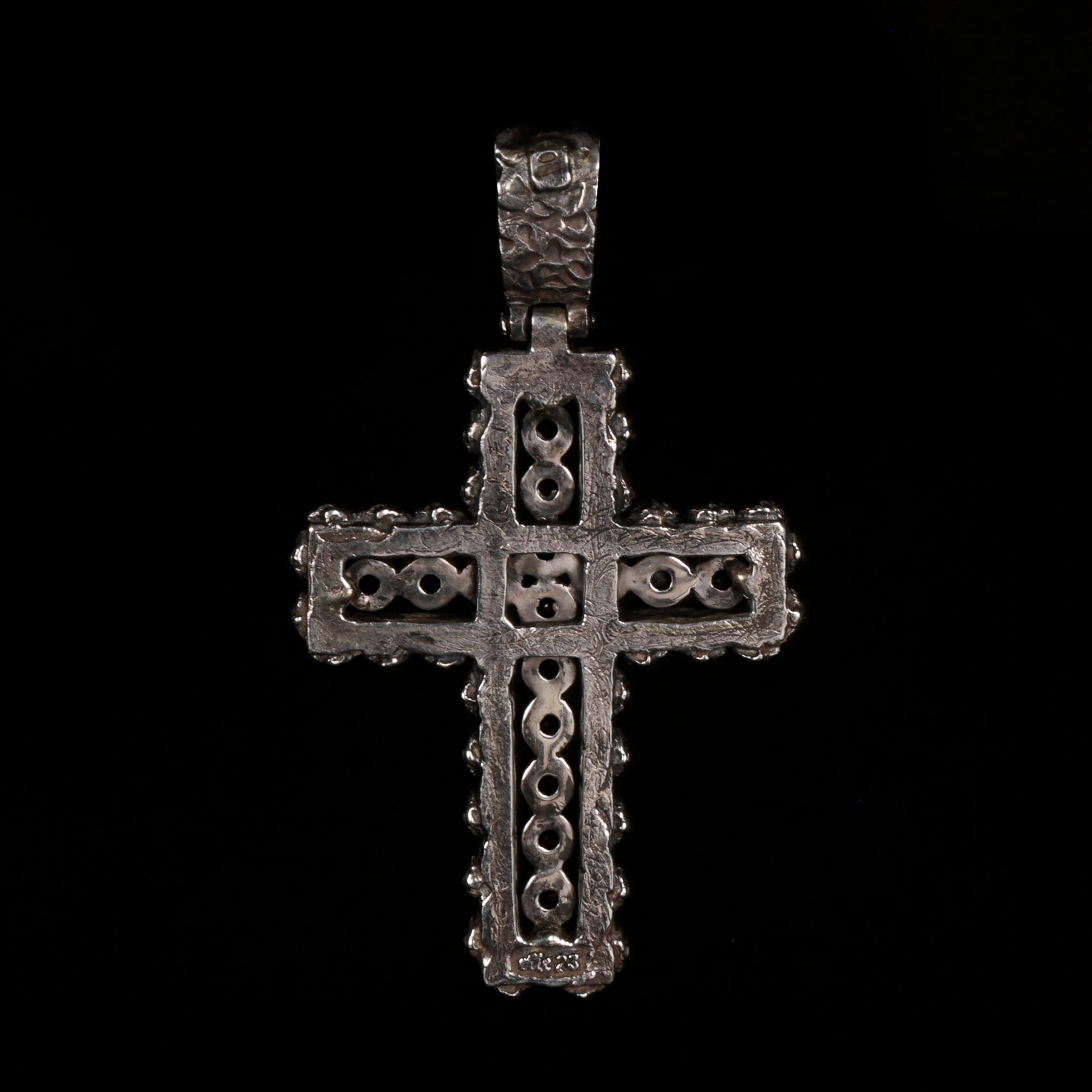 Crux Reliqvia e' un pendente a forma di croce con superficie scalfita irregolare, micro teschi saldati lungo lo spessore e incastonati granati naturali in tutta lunghezza e largezza.