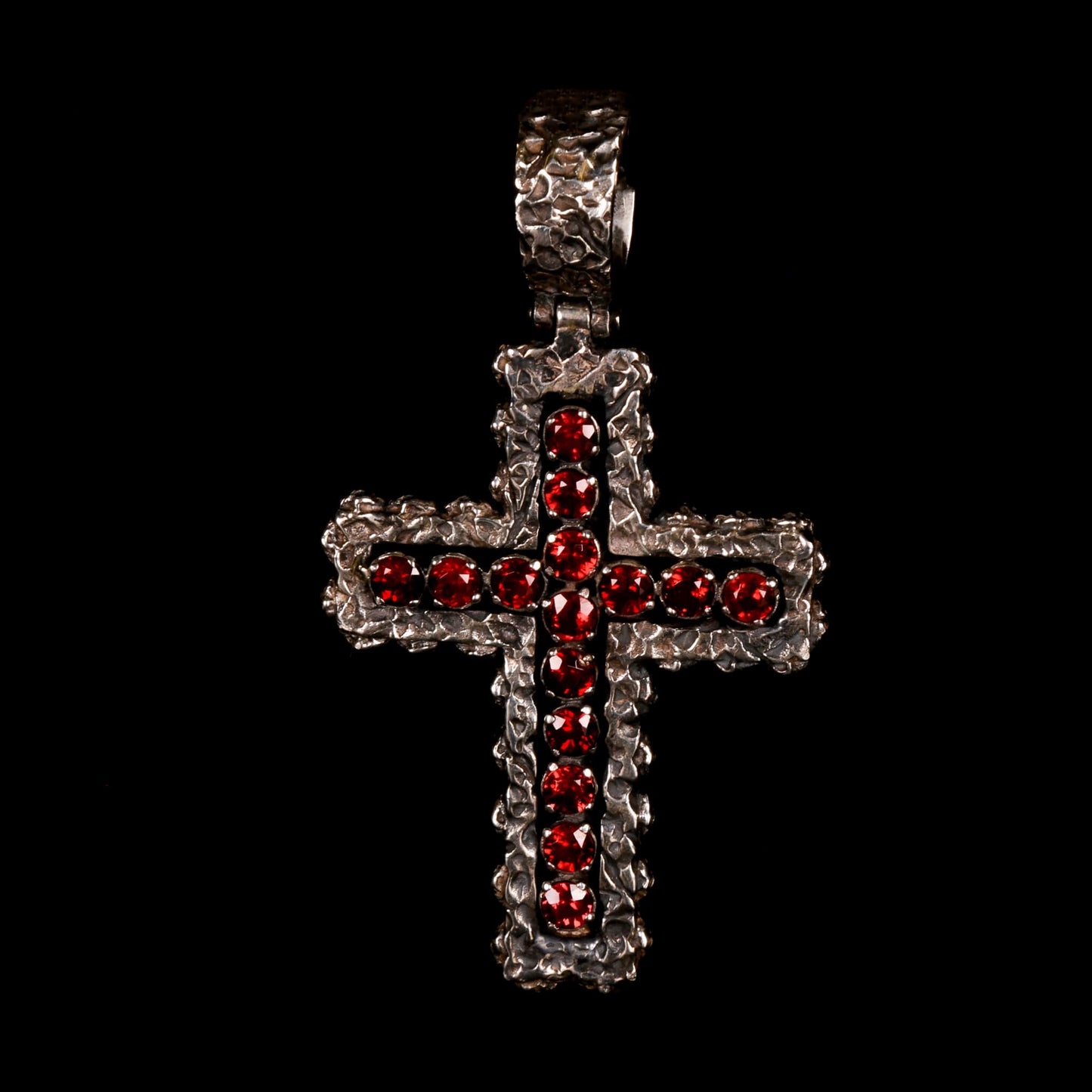 Crux Reliqvia e' un pendente a forma di croce con superficie scalfita irregolare, micro teschi saldati lungo lo spessore e incastonati granati naturali in tutta lunghezza e largezza.