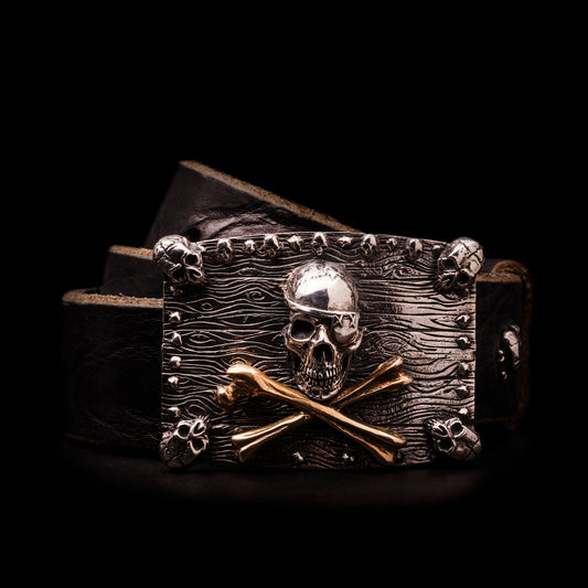 Fibbia in argento925 con teschio centrale bendato e ossa incrociate in ottone. Quattro piccoli teschi agli angoli delle tavole di legno che compongono la base della fibbia.