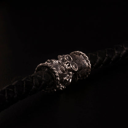 Catena portafoglio con cordino in pelle nera intrecciata ed elementi in argento925 impreziositi con teschi,croci gotiche e cuori votivi. Moschettone impreziosito con piccoli teschi e con targjetta con ala e ruota e teschio con granati.