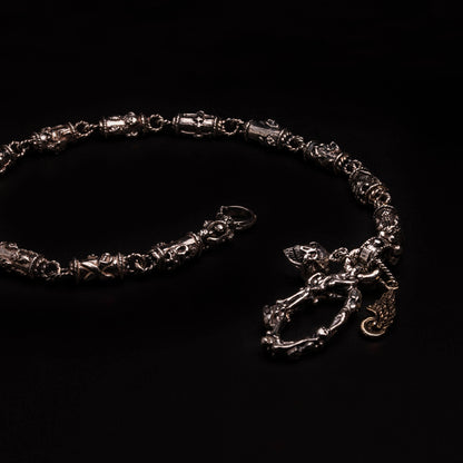 Catena portafoglio n argento925 con elementi tubolari decorati con teschi, cuori votivi, croci gotiche. Moschettone composto da ossa incrociate e teschi, con targhetta ruota e ala e teschio.