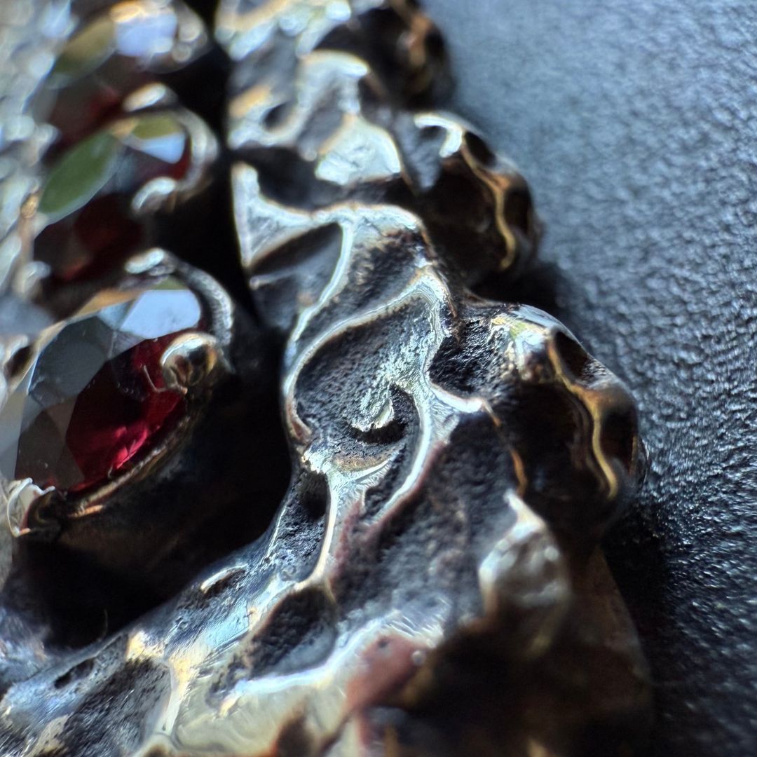 Crux Reliqvia e' un pendente a forma di croce con superficie scalfita irregolare, micro teschi saldati lungo lo spessore e incastonati granati naturali in tutta lunghezza e largezza.