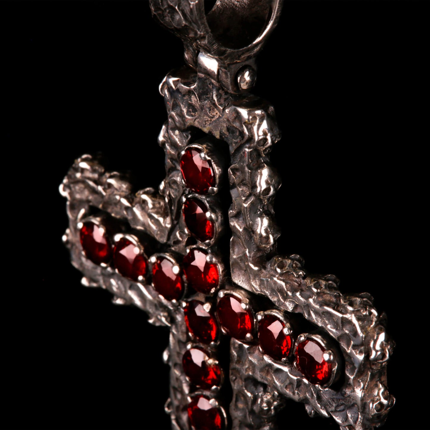 Crux Reliqvia e' un pendente a forma di croce con superficie scalfita irregolare, micro teschi saldati lungo lo spessore e incastonati granati naturali in tutta lunghezza e largezza.